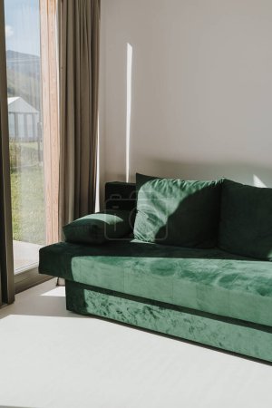 Photo for Green velour sofa in soft sunlight shadows near window. Minimalist modern home interior with furniture - Royalty Free Image