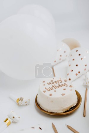 Foto de Tarta de cumpleaños, velas, globos, sombreros de fiesta sobre fondo blanco. Colores blanco y dorado - Imagen libre de derechos