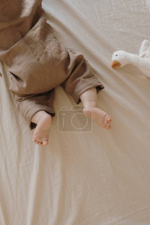 Téléchargez les photos : Vue du dessus du nouveau-né couché sur le lit. Mignon costume confortable en lin, canard jouet. Petit concept de mode bébé - en image libre de droit