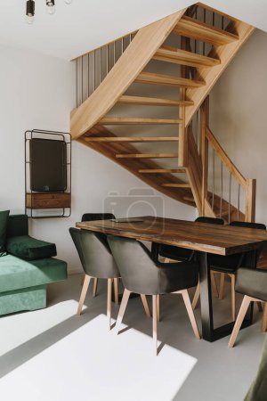 Foto de Interior de la casa moderna con sofá, escalera, mesa, sillas de espejo. Sombras de luz solar. Concepto de diseño de interiores. Apartamento en alquiler - Imagen libre de derechos