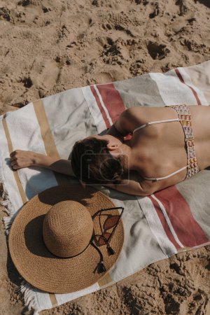 Foto de La mujer yace en la arena de playa. Sombrero de paja, gafas de sol, toalla de playa. Vacaciones de verano. Concepto estético de moda de verano - Imagen libre de derechos