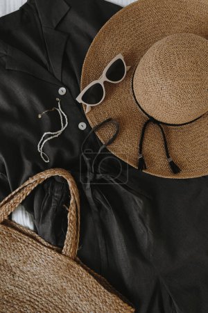 Téléchargez les photos : Composition féminine de mode d'été avec costume de lin noir, lunettes de soleil, chapeau de paille, sac en rotin sur tissu de mousseline blanche. Pose plate, vue sur le dessus collage minimaliste des vêtements. Blog de mode féminine, médias sociaux - en image libre de droit