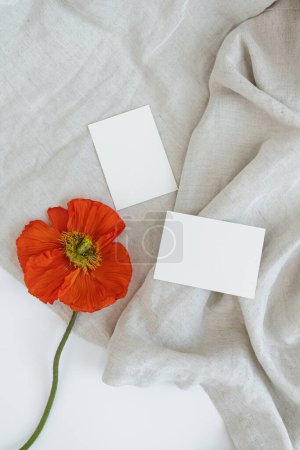 Téléchargez les photos : Cartes de feuille de papier vierges avec espace de copie maquette et fleur de pavot sur tissu froissé. Modèle de marque d'entreprise minimale. Couché plat, vue du dessus - en image libre de droit
