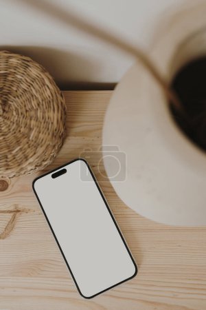 Foto de Teléfono móvil con pantalla en blanco, ataúd de ratán en mesa de madera. Plantilla estética neutra beige para redes sociales, sitio web móvil con espacio de copia para maqueta. Piso tendido, vista superior - Imagen libre de derechos