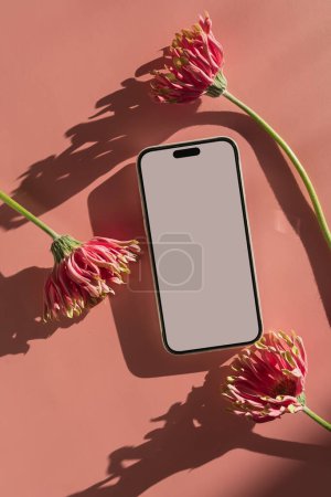 Téléchargez les photos : Smartphone avec écran blanc et fleurs gerbeuses sur fond rose. Ombres solaires esthétiques. Modèle de marque d'entreprise minime avec espace de copie de maquette - en image libre de droit