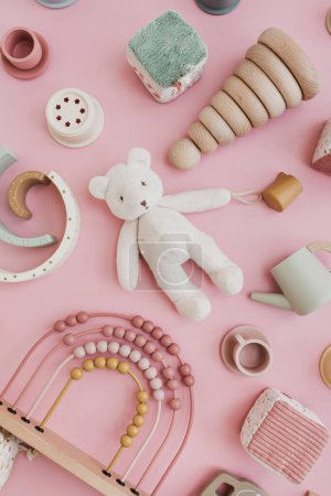 Baby kids toys background. Teddy bear, wooden educational stacking rainbow, pyramid, toy kitchenware on pastel pink background. Top view, flat lay