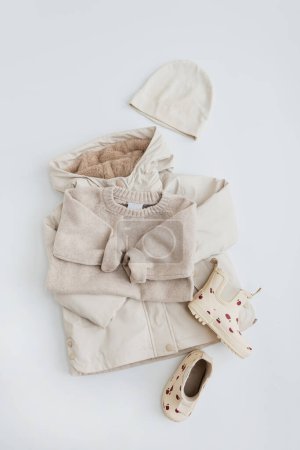 Photo for Set of neutral beige colour children's warm clothes for rainy weather. Kids sweater, raincoat, rubber rain boots, hat on white background. Flat lay, top view Scandinavian nordic baby fashion collage - Royalty Free Image