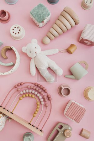 Set of stylish natural Scandinavian baby kids toys on pastel pink background. Baby girl stuff for playing and education. Flat lay, top view