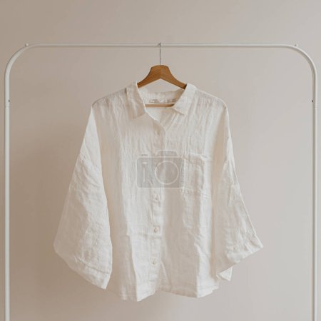 Téléchargez les photos : Chemise froissée blanche, chemisier sur cintre au-dessus du mur blanc. Esthétique vêtements de mode féminine, concept de garde-robe - en image libre de droit