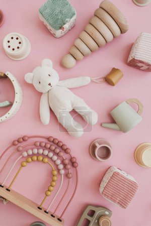 Baby toddler organic natural wooden toys on pastel pink background. Stacking cups, rainbow, kitchenware, teddy bear. Flat lay, top view