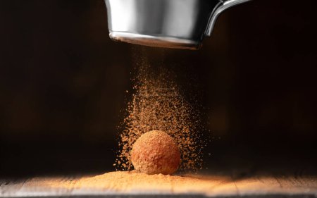 Photo for A ball of chocolate truffle is sprinkled with cocoa from a strainer on a dark background close-up. Chocolate Fiery. Conceptual photo of a gourmet truffle. - Royalty Free Image