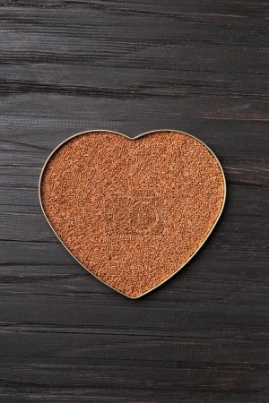 Foto de Chocolate chips are poured into a heart-shaped box on a wooden background with space for text. Milk chocolate in the shape of a heart on a dark background top view. Valentine's Day. - Imagen libre de derechos