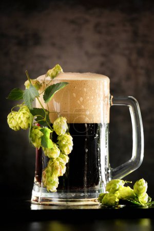 Téléchargez les photos : Dark beer in a mug and green hop on wooden table on brown background. Oktoberfest. Beer Festival. - en image libre de droit