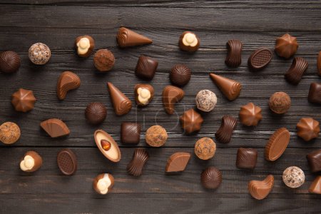 Photo for Different chocolate candies on a dark wooden texture background top view. Assorted sweets on the table. Dark and milk chocolates. Chocolate dessert. Candy flat lay. - Royalty Free Image