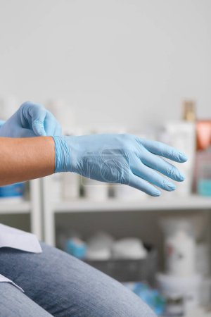 Ärztinnen ziehen blaue sterilisierte OP-Handschuhe an. Sterilität, Sicherheit. Pandemiezeit, Quarantäne. Operationen, Kosmetik, Maniküre. Chirurg, Kosmetologe.