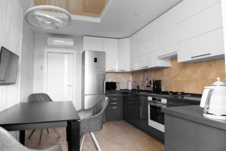 Téléchargez les photos : The kitchen in the apartment The design of the kitchen room. Black dining table in the kitchen. Gray kitchen interior with white cabinets. Built-in oven in the interior of the kitchen Kitchen interier - en image libre de droit