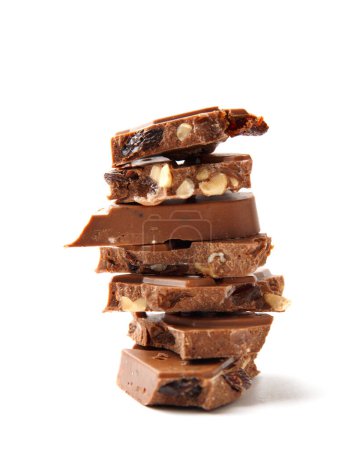 Foto de Pieces of chocolate with nuts and raisins are stacked on a white background close-up. Broken chocolate lies in a pile on insulation. Chocolate slices with crushed nuts and dry grapes macro shot. - Imagen libre de derechos
