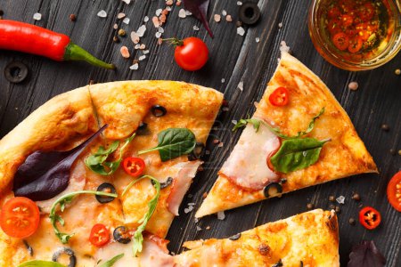 Photo for Pizza with salami, olives, cheese and herbs, sauce, olive oil with spices and fresh vegetables on a dark wooden background top view. Homemade pizza with meat. Traditional Italian food. - Royalty Free Image