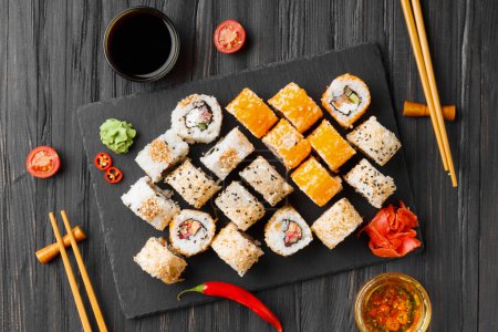 Téléchargez les photos : Ensemble de rouleaux de saumon sur un fond sombre avec baguettes, sauce et gingembre rouge vue du dessus. Sushi rouge au sésame sur fond noir. - en image libre de droit