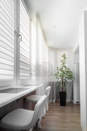Téléchargez les photos : Modern trendy interior of the loggia. White bar stools, a bar counter, a flower in a large flowerpot, gray blinds on the windows, laminate on the wall of the apartment's closed balcony. - en image libre de droit