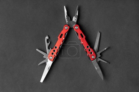 Téléchargez les photos : Universal multifunctional knife pliers with different nozzles and a red handle on a dark gray background. Versatile camping knife. Multifunctional tool. - en image libre de droit