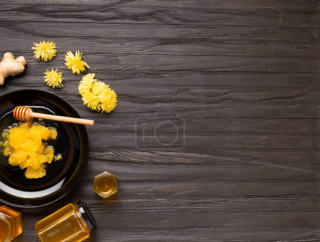 Téléchargez les photos : Conceptual composition of crystallized honey in a black plate, liquid flower honey in jars, lemon, lime, ginger on a dark background top view with space for text. Different honey on a black background. - en image libre de droit