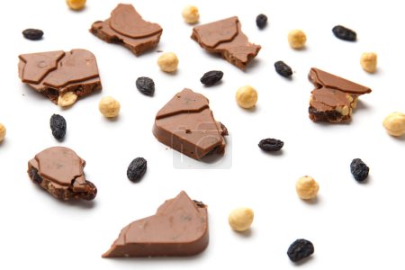 Téléchargez les photos : Pieces of broken chocolate bar, hazelnuts, raisins are scattered on a white background. Milk chocolate with nuts and dry grapes isolated. - en image libre de droit