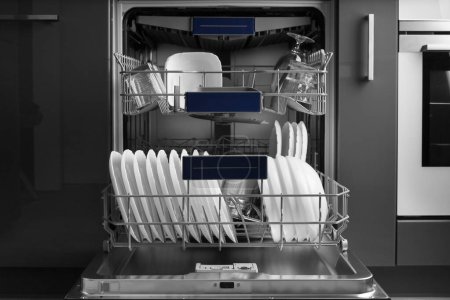 Téléchargez les photos : Built-in dishwasher in the kitchen with the door open and clean dishes inside. Clean white plates, saucepan, glasses are stacked inside the dishwasher. Household appliances for the kitchen. - en image libre de droit