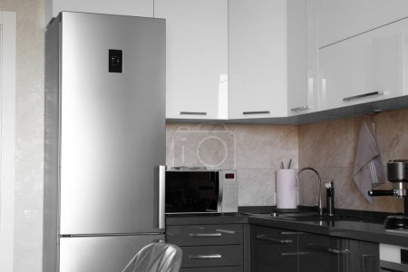 Téléchargez les photos : Kitchen in the apartment Design of the kitchen room. Gray kitchen interior with white cabinets. Refrigerator and microwave in stainless steel in the interior of the kitchen. - en image libre de droit