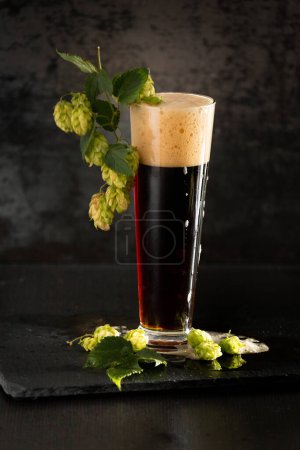 Photo for Dark beer in a mug and green hop on wooden table on brown background. Oktoberfest. Beer Festival. - Royalty Free Image