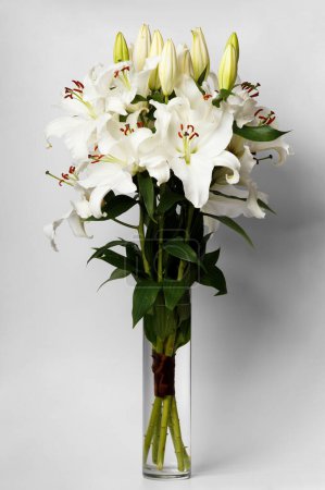 Foto de Gran ramo de flores de lirios blancos en un jarrón de vidrio sobre un fondo blanco. Lirios blancos en un jarrón aislado - Imagen libre de derechos