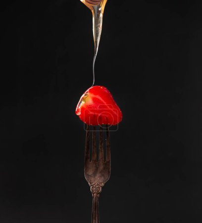 Téléchargez les photos : Half of a strawberry on an old fork on a dark background close-up. Honey flows over strawberries. - en image libre de droit