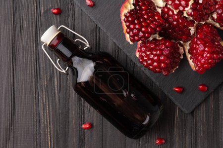 Photo for Pomegranate, scattered pomegranate seeds and pomegranate juice on a dark wooden background top view. Freshly squeezed pomegranate juice in a glass bottle on a stone plate and a broken pomegranate. - Royalty Free Image