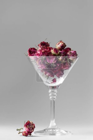 Téléchargez les photos : Buds of pink roses in a martini glass isolated. Buds of dried flowers in a glass goblet on a white background. Dried flower tea. Valentine's Day. - en image libre de droit