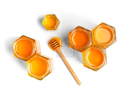 Creative composition of honey in open jars in the form of honeycombs and a wooden dipper on a white background top view. The concept of organic bee products. Honey on isolation.
