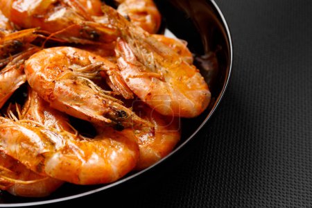 Téléchargez les photos : Crevettes frites dans une assiette noire sur une table en céramique sombre close-up. Grill de crevettes sur un fond sombre. - en image libre de droit