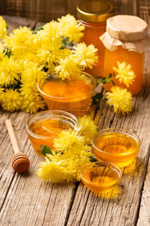 Téléchargez les photos : Composition of honey in bowls of different sizes, wooden dipper and yellow flowers on an aged wooden background close-up. Healthy food. Still life of honey and flowers. - en image libre de droit