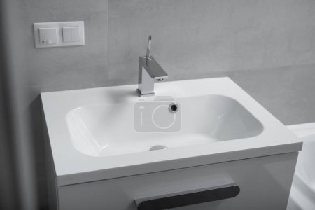 Foto de Moderno cuarto de baño interior, lavabo blanco con cajones, grifo de cromo, zócalo y interruptor en la pared. Interior del baño con lavabo y grifo. - Imagen libre de derechos