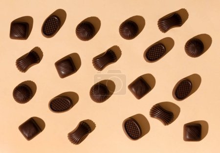 Téléchargez les photos : Bonbons au chocolat sur fond beige vue du dessus, fond sucré de chocolats de différentes formes - en image libre de droit