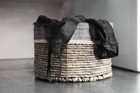 Photo for Conceptual composition, women's underwear in a wicker basket for dirty laundry on a black background. A filled laundry basket against a dark floor. - Royalty Free Image