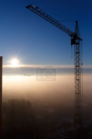 Photo for Construction crane in the fog in the morning. Sunrise, morning fog, construction site, tower crane. Mystical foggy morning in the city at dawn. Urban landscape. - Royalty Free Image