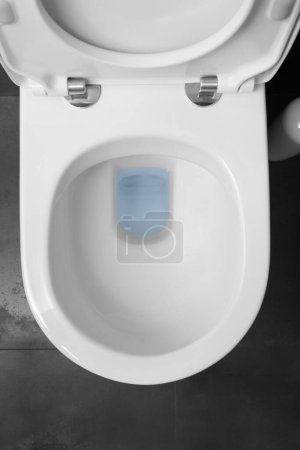 Photo for Top view of a white toilet bowl with a raised lid against a black ceramic floor. - Royalty Free Image