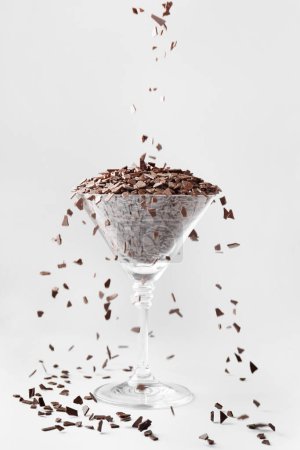 Photo for Creative composition, chocolate chips are poured into a martini glass isolated on a white background. Chocolate cocktail. - Royalty Free Image