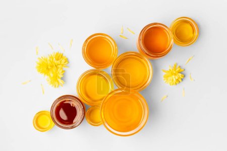 Foto de Miel en cuencos de vidrio de diferentes tamaños en una vista superior de fondo blanco. Composición creativa de tarros de miel en aislamiento. - Imagen libre de derechos
