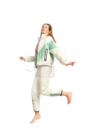 Foto de Una chica en un chándal ligero de moda para un paseo posa sobre un fondo blanco descalzo, publicidad de ropa, estilo callejero, ropa casual con estilo cómodo. - Imagen libre de derechos
