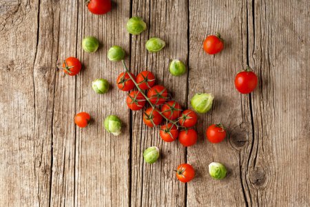 Foto de Pequeños tomates cherry y coles de Bruselas sobre un fondo de madera envejecida. Mezcla de verduras frescas y saludables. Un símbolo de una nutrición adecuada y saludable. - Imagen libre de derechos