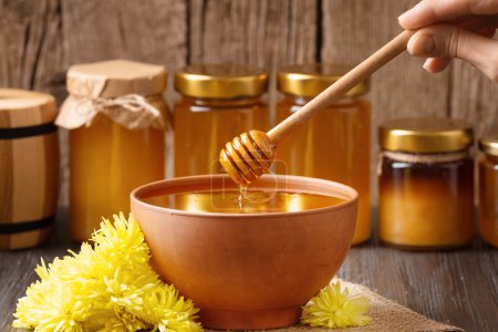 Téléchargez les photos : Composition créative de bocaux au miel, miel dans un bol en argile, trempette et verser le miel sur un fond en bois. Le miel est versé d'une cuillère en bois dans un bol en céramique. - en image libre de droit