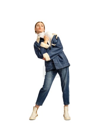 Téléchargez les photos : Une jeune fille dans une veste et un jean en cuir denim élégant pose magnifiquement sur un fond blanc. Des vêtements confortables et élégants pour la ville. - en image libre de droit