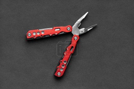 Foto de Universal multifunctional knife pliers with different nozzles and a red handle on a dark gray background. Versatile camping knife. Multifunctional tool. - Imagen libre de derechos