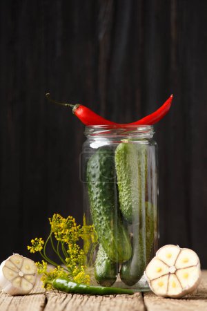 Photo for Fresh cucumbers in a glass jar for home canning, chili peppers, dill, garlic on an old wooden background. Gherkins and spices for homemade marinade. - Royalty Free Image